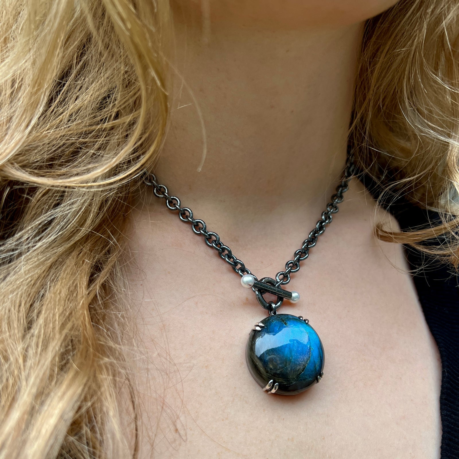 A globe-like labradorite pendant on a cable chain with pearl toggle worn by a person