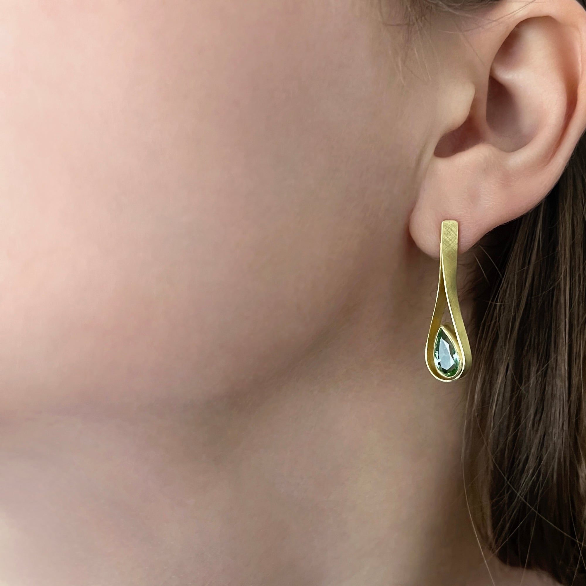 Gold earring with a mint tourmaline teardrop-shaped gemstone worn by a person.