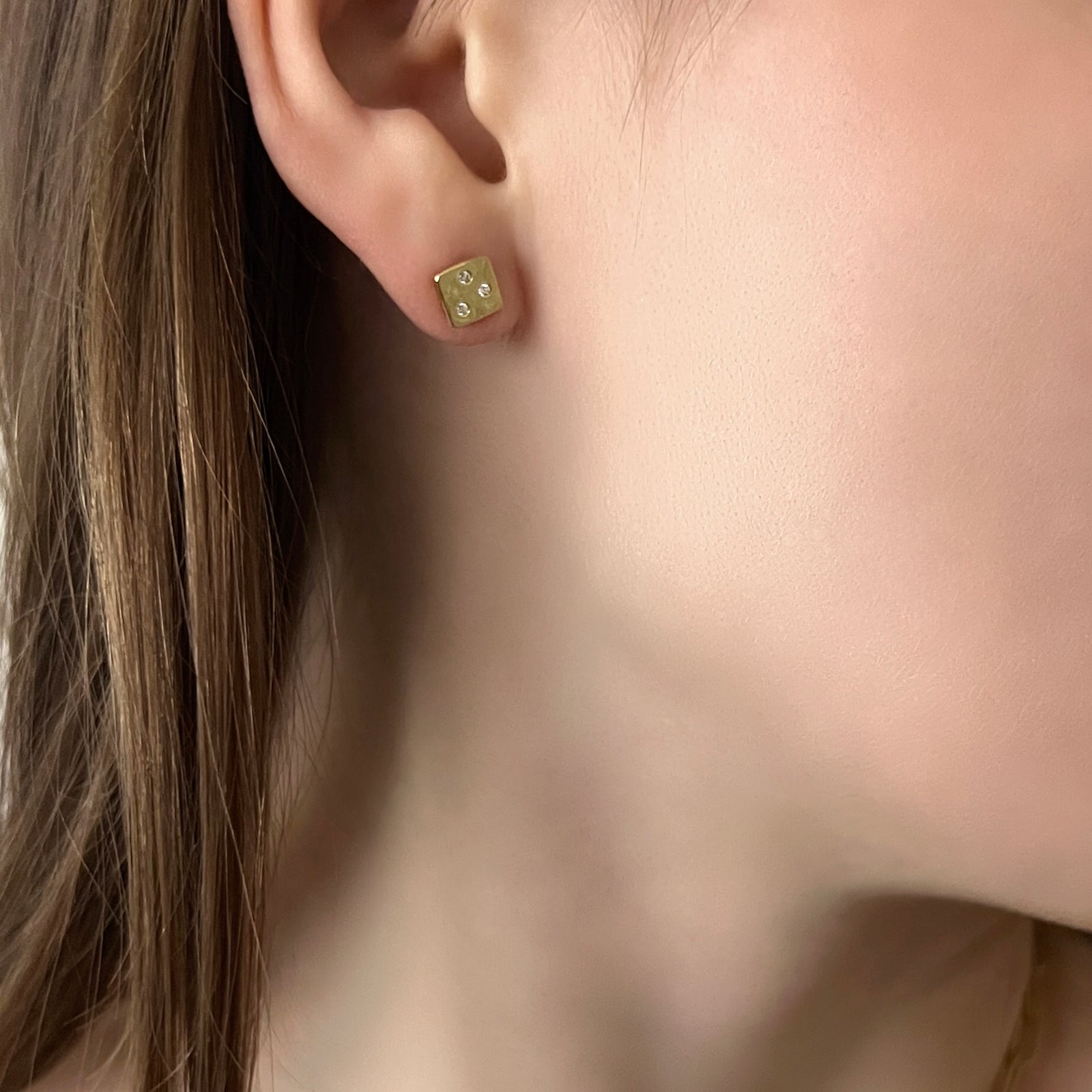 Gold earring stud with three small diamonds worn by a person