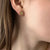 Gold earring stud with three small diamonds worn by a person