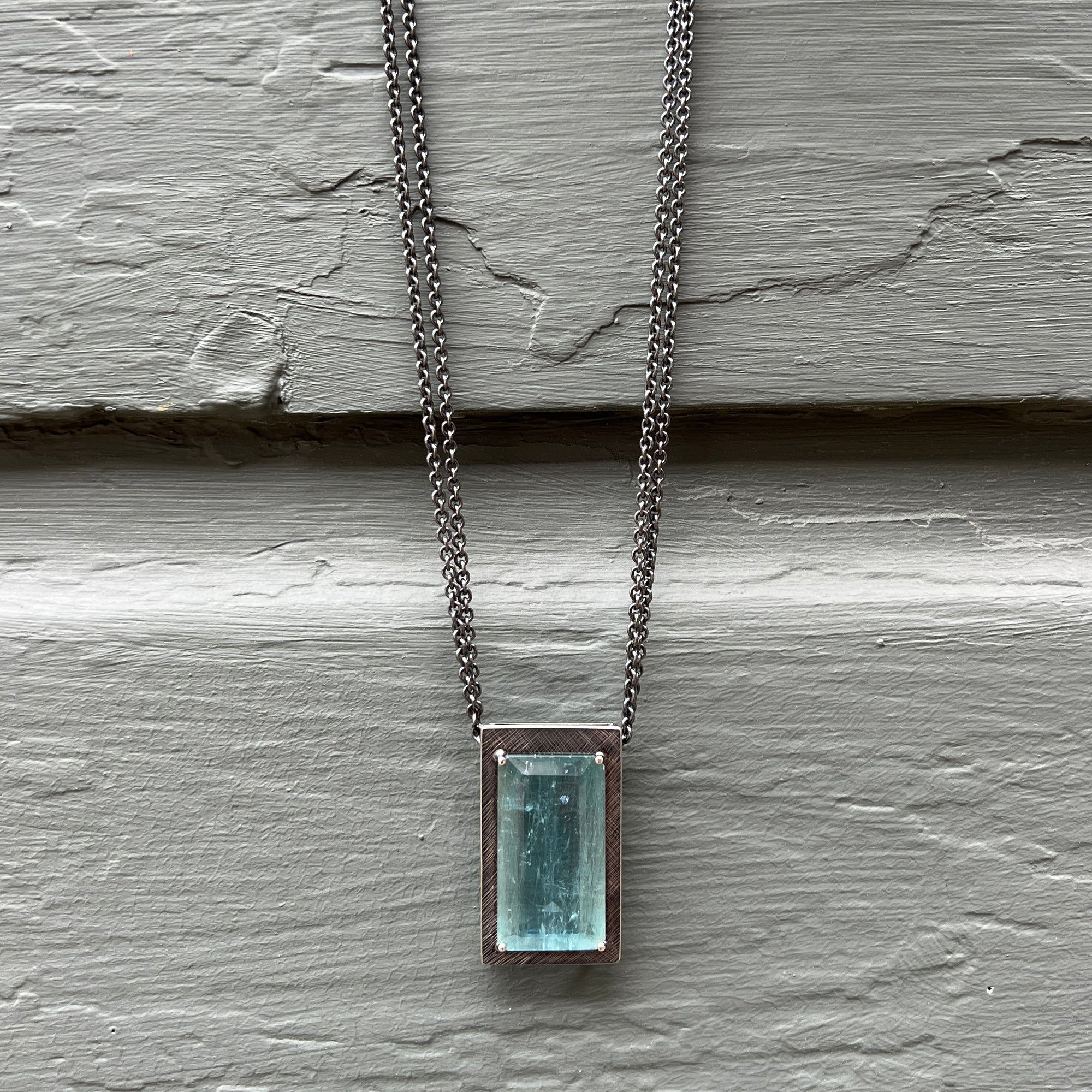 A dynamic, emerald-cut aquamarine pendant on long sterling chain