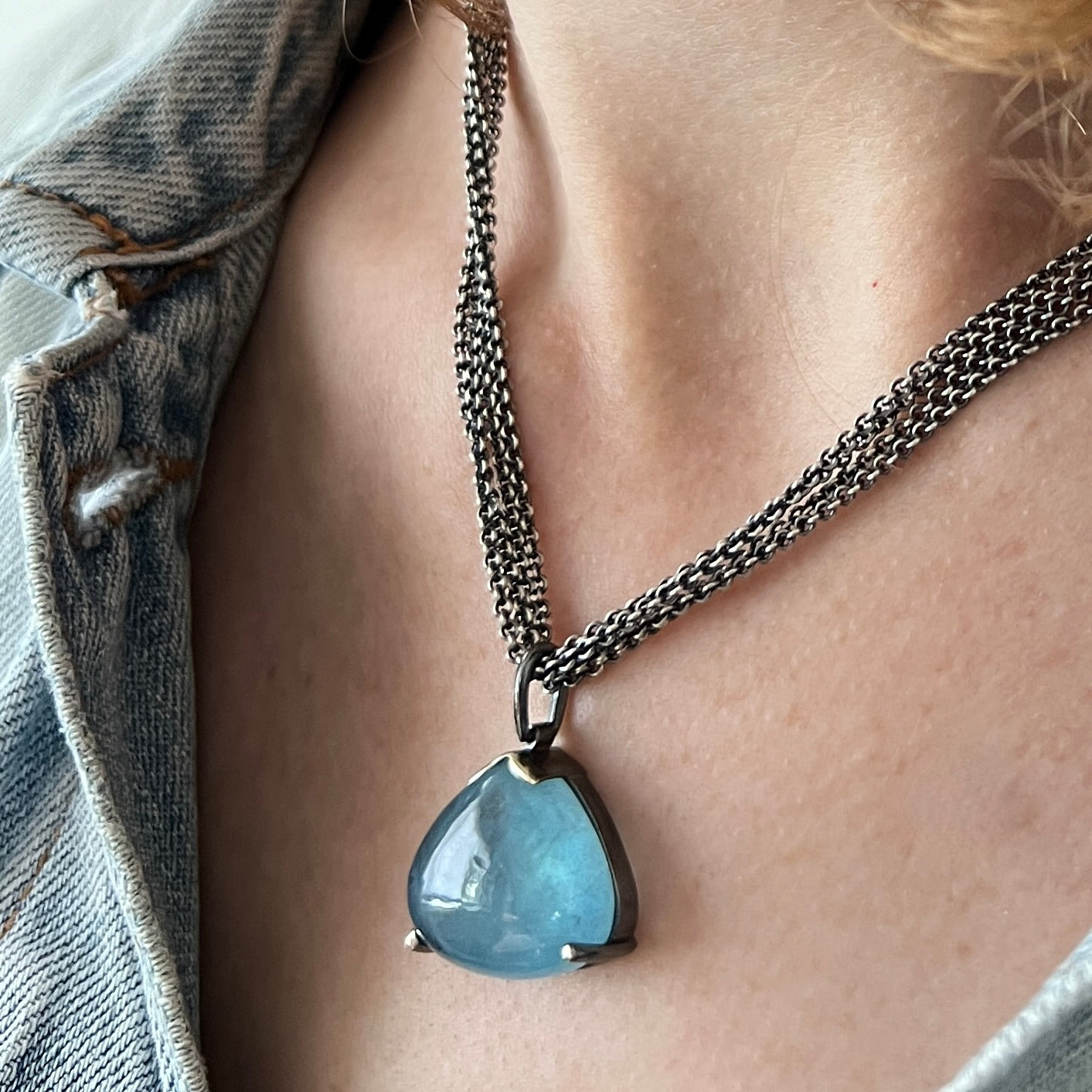 A luscious triangular aquamarine cabachon pendant is hanging from a multi-strand chain. Made by Ayesha Mayadas