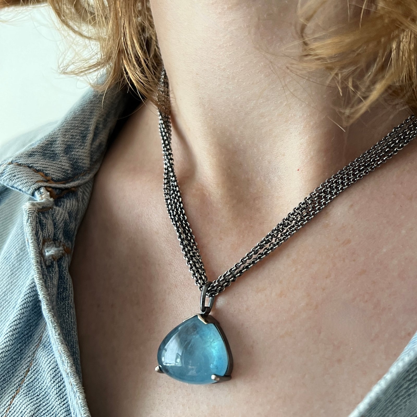 A luscious triangular aquamarine cabachon pendant is hanging from a multi-strand chain. Made by Ayesha Mayadas