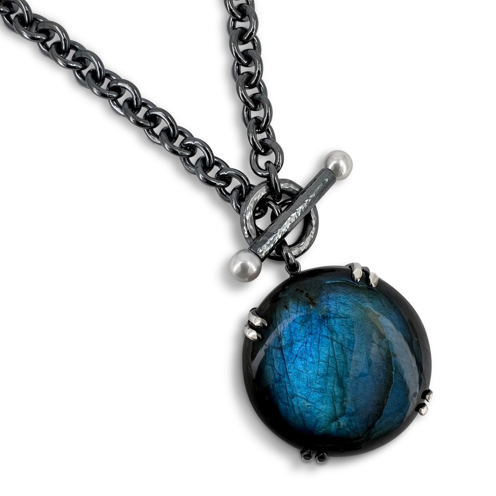 A globe-like labradorite pendant on a cable chain with pearl toggle worn by a person