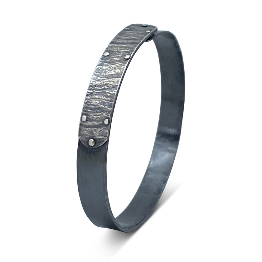 Narrow forged cuff bracelet with wafer texture studded tab in sterling silver with top closure by Ayesha Mayadas